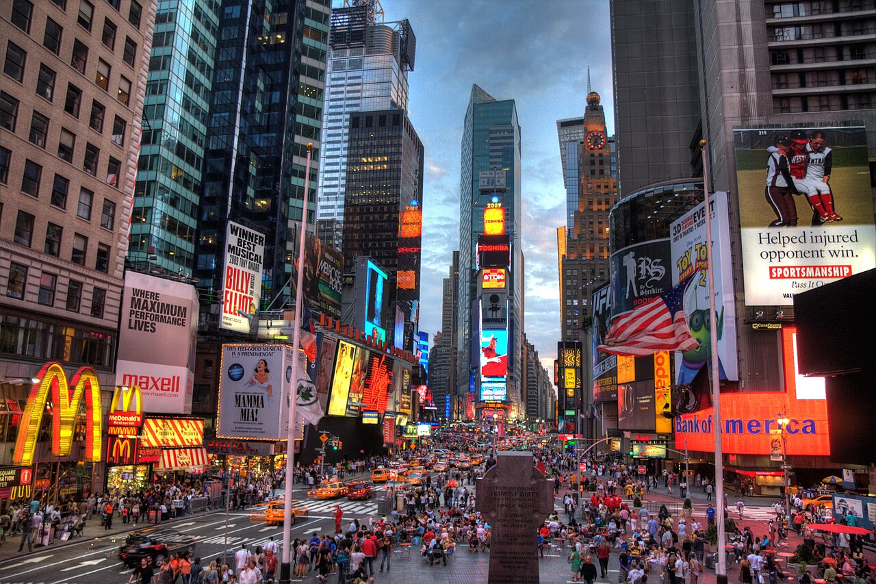 Crowds and traffic in Times Square beneath illuminated advertisements and theatre billboards.. Photo: